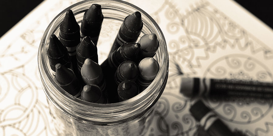 a glass jar containing crayons, with a couple more crayons laying on a drawing